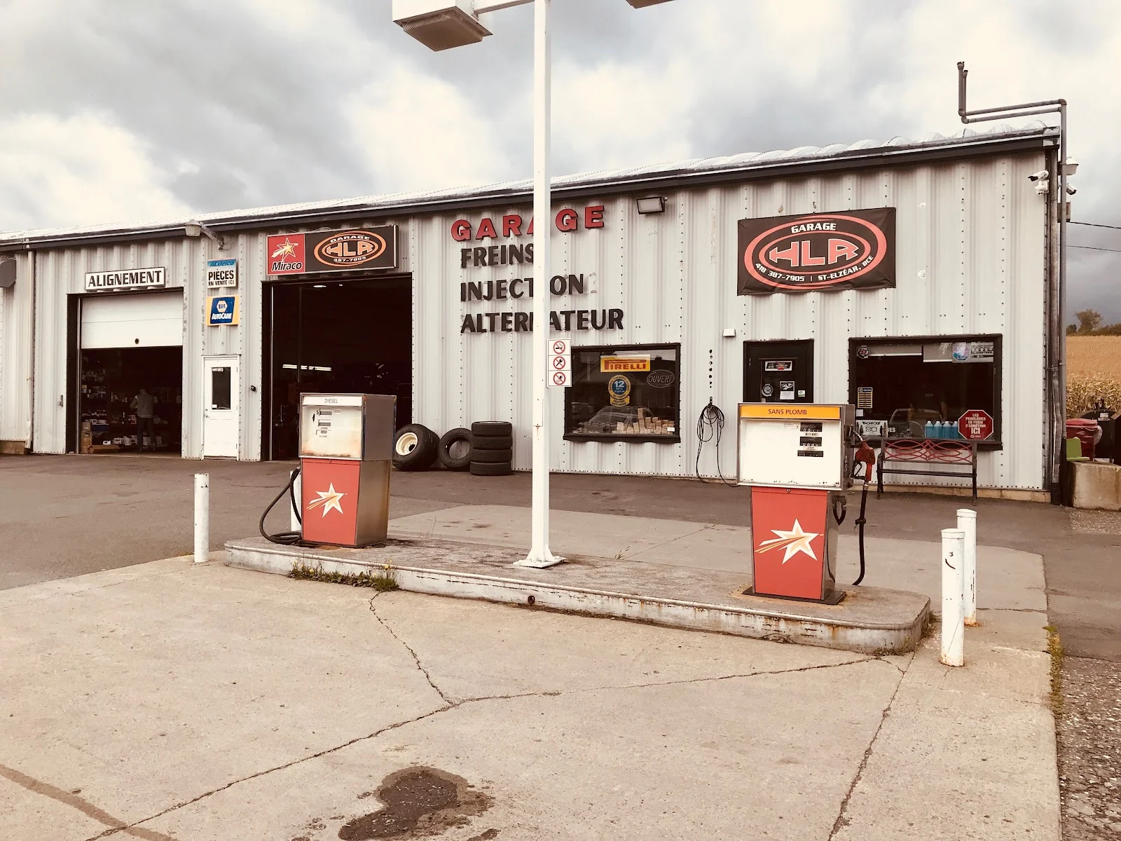 Devanture du garage : bardage de tôle, trois portes de baie dont une marquée « Alignement », deux pompes à essence et la bannière HLR.