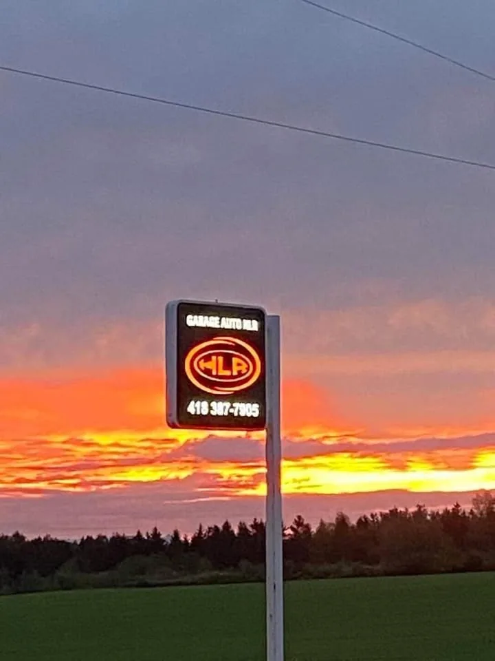 Enseigne lumineuse « Garage Auto HLR » et son numéro de téléphone, en bordure de route au coucher du soleil.